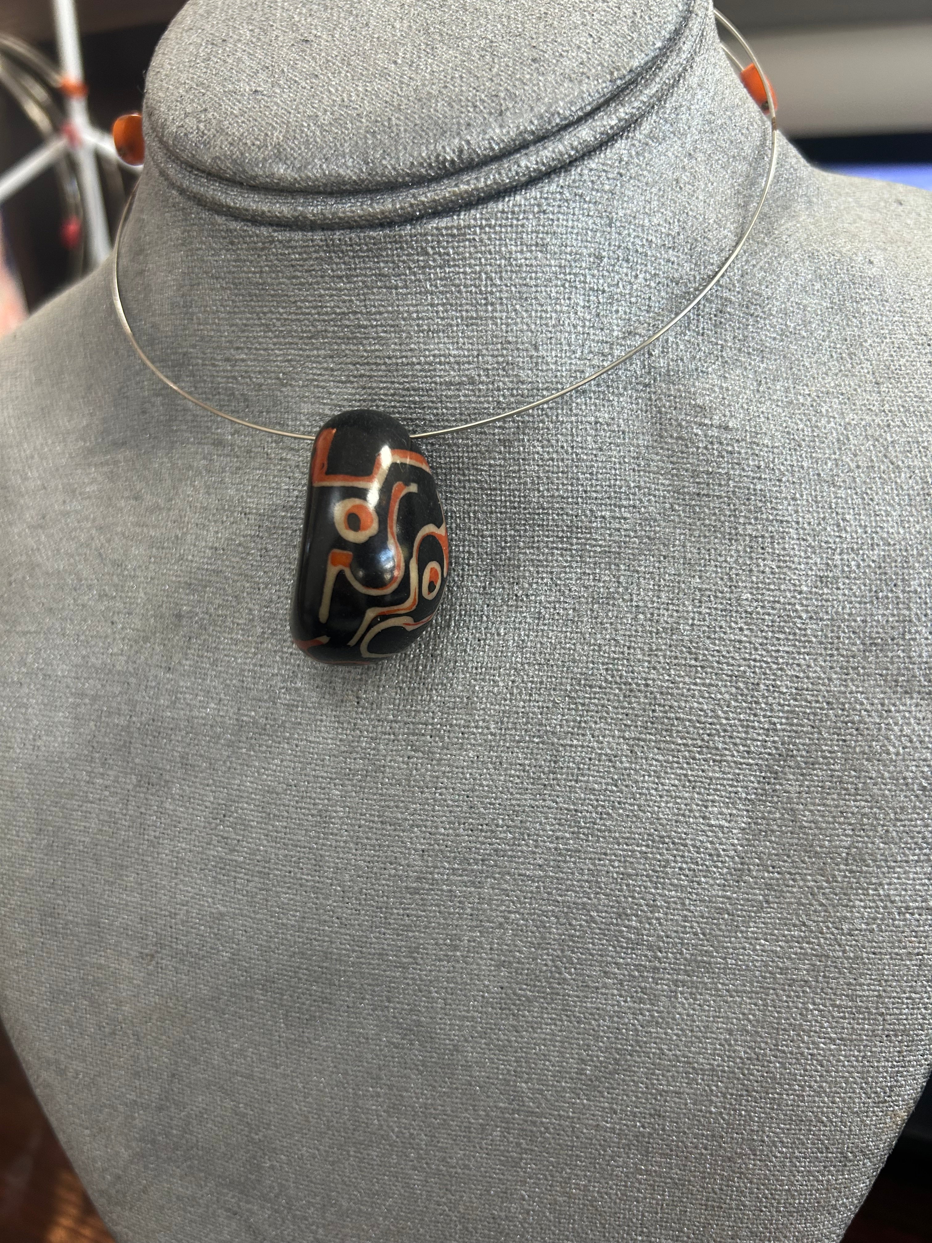 Collar con dije de piedra pulida en negro intenso decorado con detalles artesanales en tonos terracota y marfil.