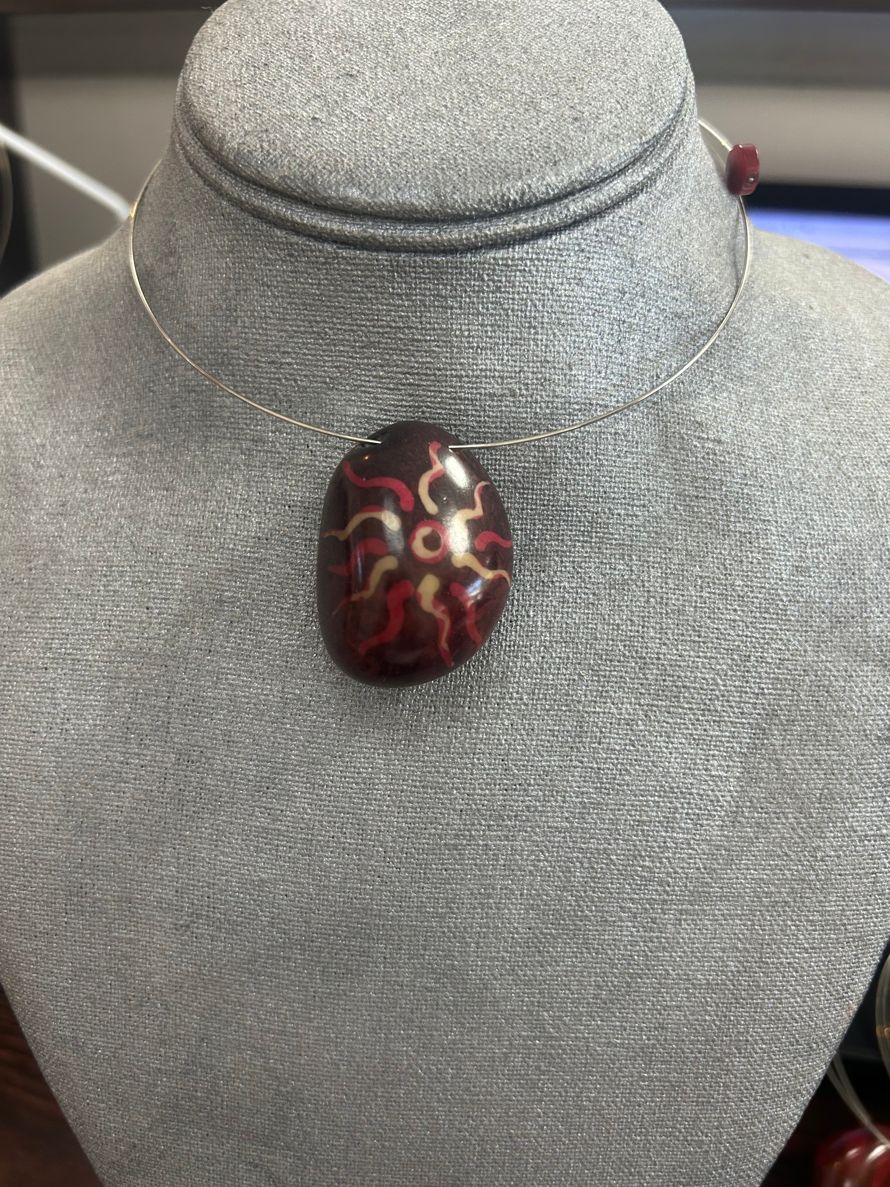 Collar con dije de piedra pulida en tono vino profundo decorado con detalles orgánicos en rojo y marfil