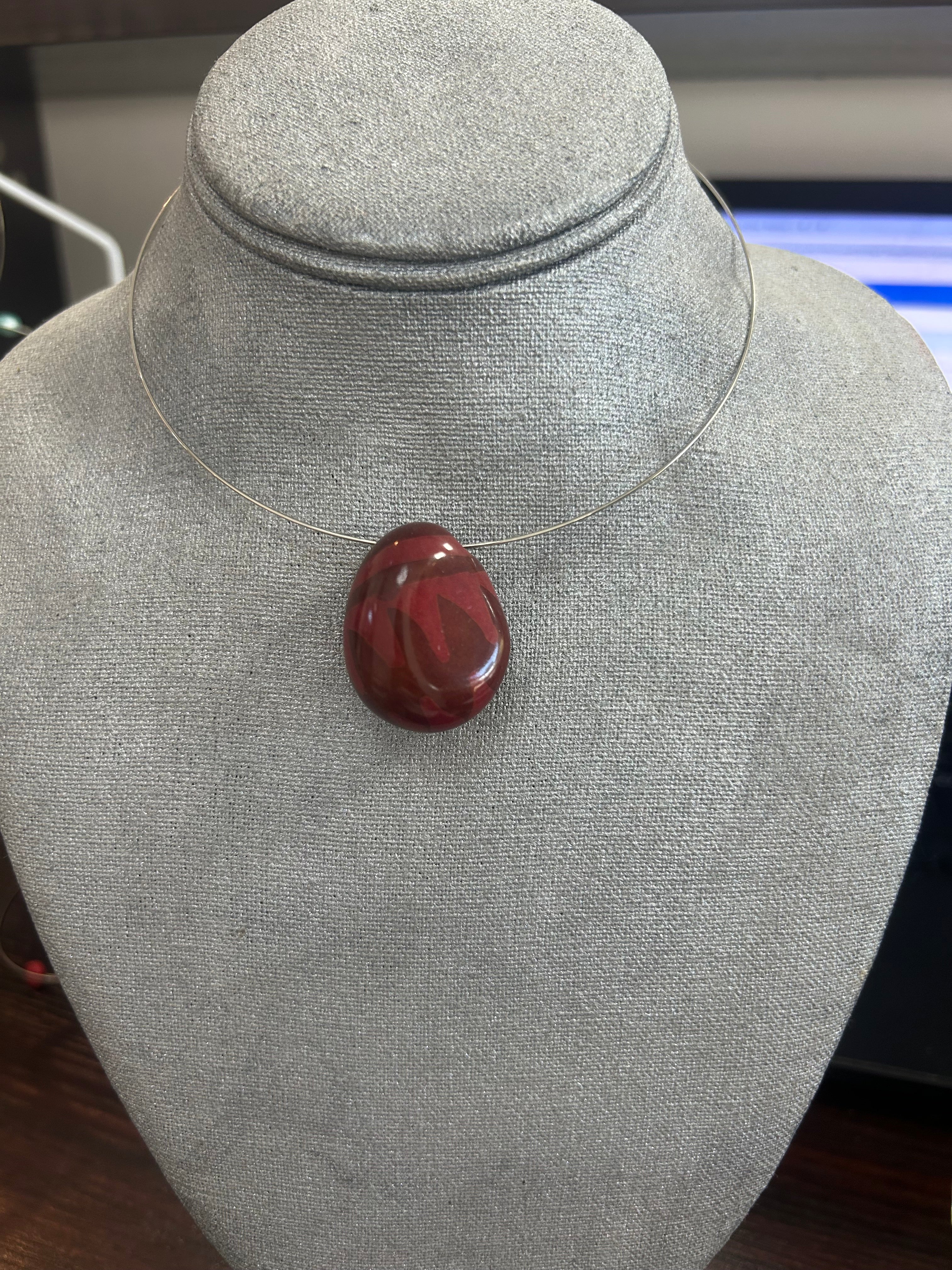 Collar con dije de piedra pulida en tono rojo borgoña, con sutiles vetas que realzan su brillo natural.